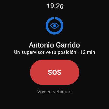 Pantalla de inicio del reloj del trabajador con el anillo de estado en azul y un ojo dentro, y debajo de su nombre la línea «Un supervisor ve tu posición · 12 min». El botón SOS sigue en su sitio, y debajo el de «Voy en vehículo»